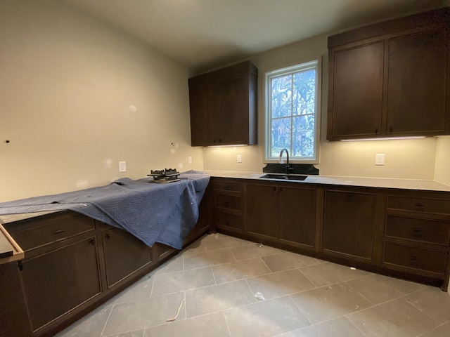 kitchen with dark brown cabinetry, sink, and light tile patterned flooring