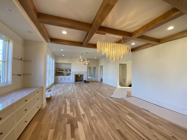 unfurnished living room featuring beamed ceiling, coffered ceiling, a chandelier, and light hardwood / wood-style floors