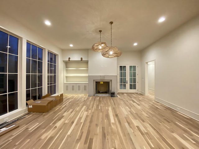 unfurnished living room with french doors, light hardwood / wood-style floors, and built in shelves