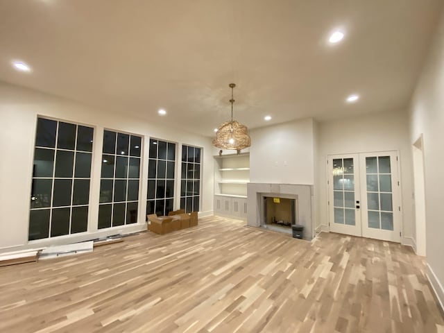 unfurnished living room with french doors, built in shelves, and light hardwood / wood-style flooring