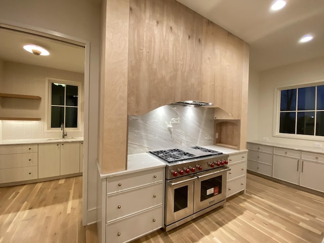 kitchen with light wood-type flooring, double oven range, sink, and backsplash