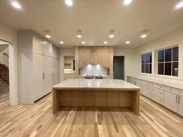 kitchen with a kitchen breakfast bar, a large island, light stone counters, and light hardwood / wood-style flooring