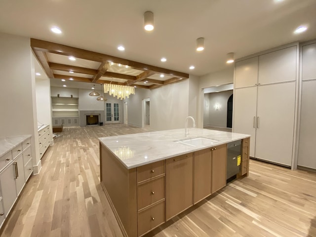 kitchen featuring sink, beam ceiling, a large island, light stone countertops, and light hardwood / wood-style floors