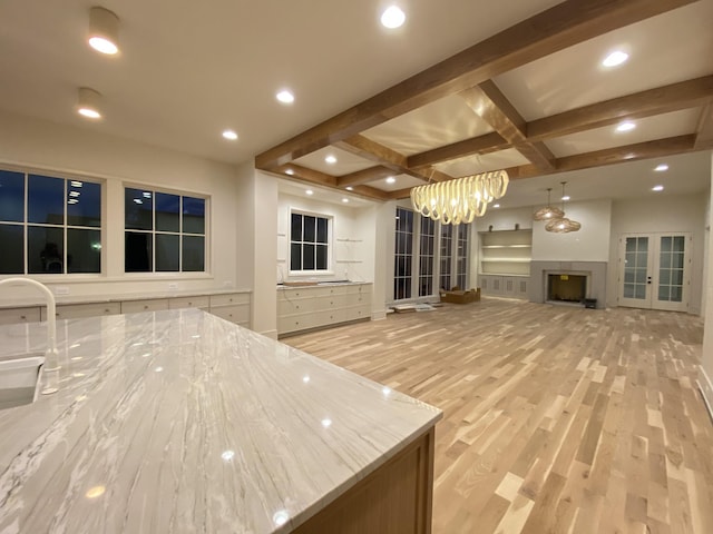 kitchen with beamed ceiling, hanging light fixtures, light hardwood / wood-style floors, and light stone counters