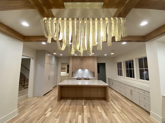 kitchen with beamed ceiling, a kitchen island, and light wood-type flooring