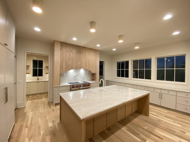 kitchen with a spacious island, a kitchen bar, sink, light stone counters, and double oven range