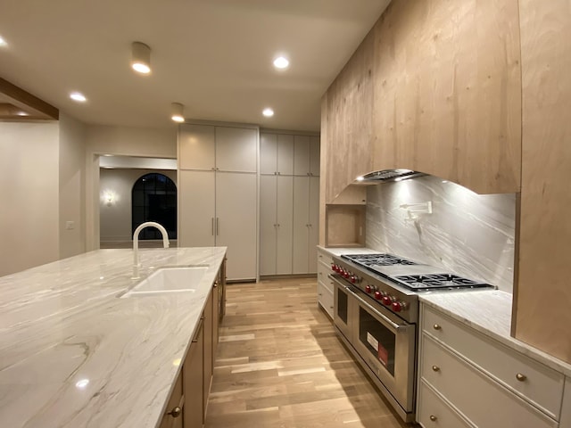 kitchen with sink, backsplash, range with two ovens, light stone counters, and light wood-type flooring