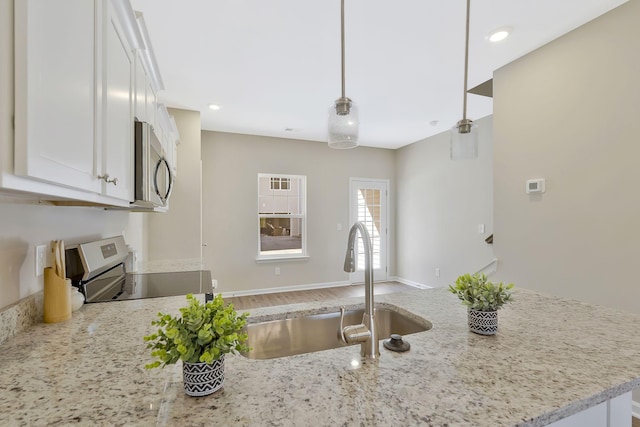 kitchen with sink, white cabinetry, light stone counters, decorative light fixtures, and stainless steel appliances