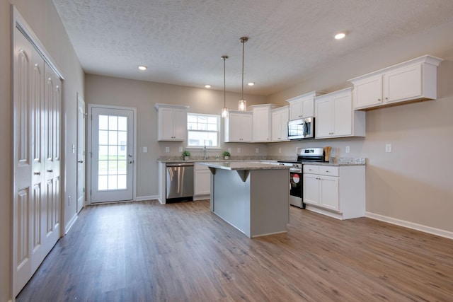 kitchen featuring a kitchen island, white cabinets, hanging light fixtures, stainless steel appliances, and light hardwood / wood-style flooring