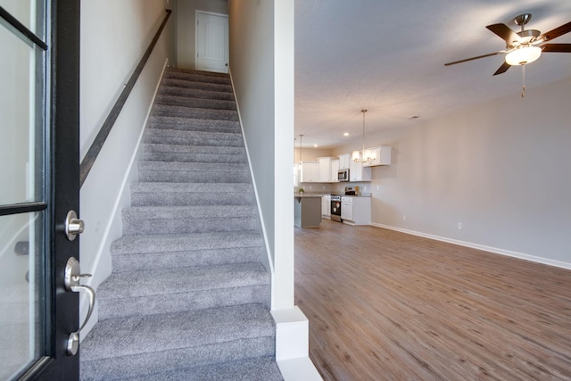 staircase with hardwood / wood-style flooring and ceiling fan with notable chandelier