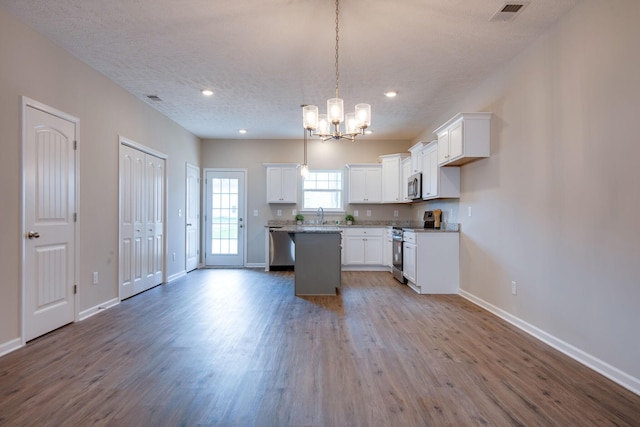 kitchen with pendant lighting, white cabinetry, hardwood / wood-style floors, stainless steel appliances, and a center island