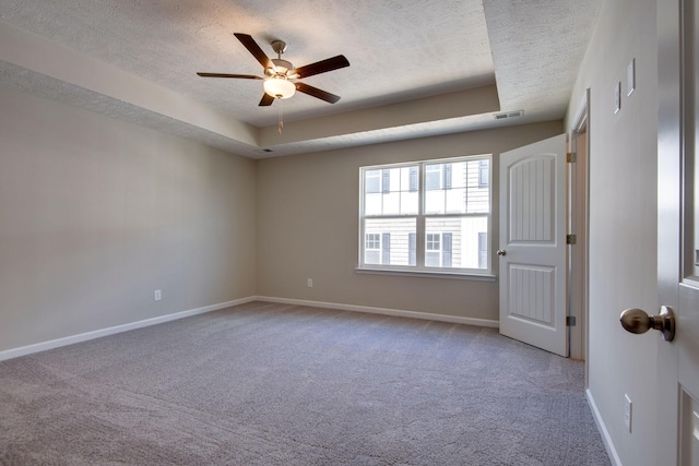 carpeted empty room with ceiling fan, a raised ceiling, and a textured ceiling