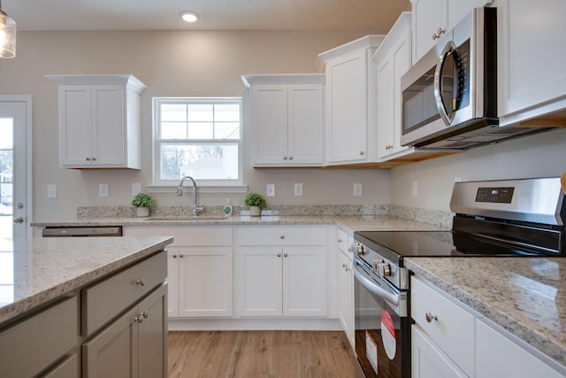 kitchen with stainless steel appliances, light stone countertops, sink, and white cabinets