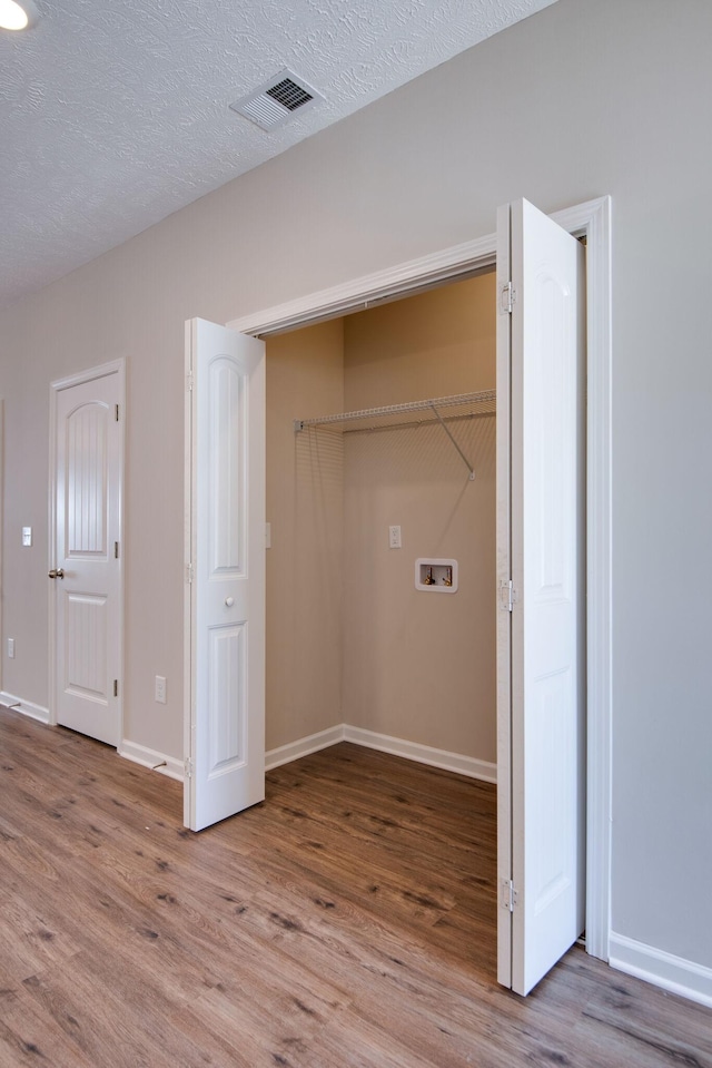 clothes washing area featuring hookup for a washing machine, light hardwood / wood-style flooring, and a textured ceiling