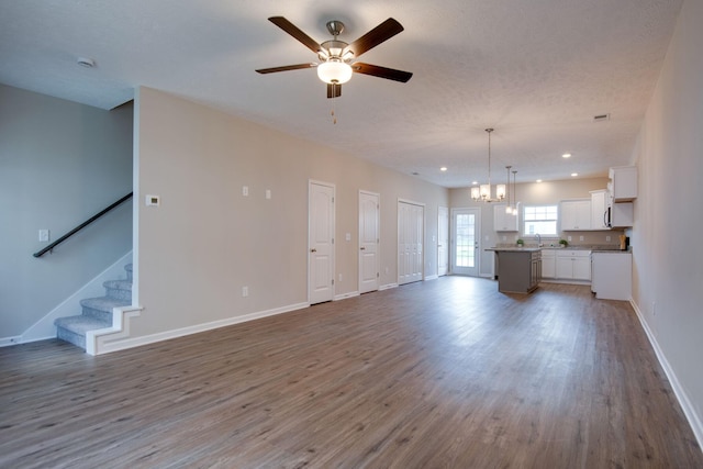 unfurnished living room featuring wood-type flooring and ceiling fan with notable chandelier