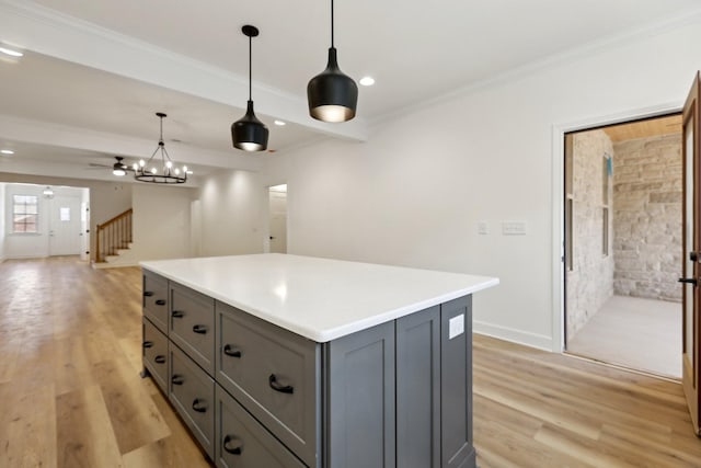 kitchen with gray cabinets, ornamental molding, a kitchen island, decorative light fixtures, and light wood-type flooring