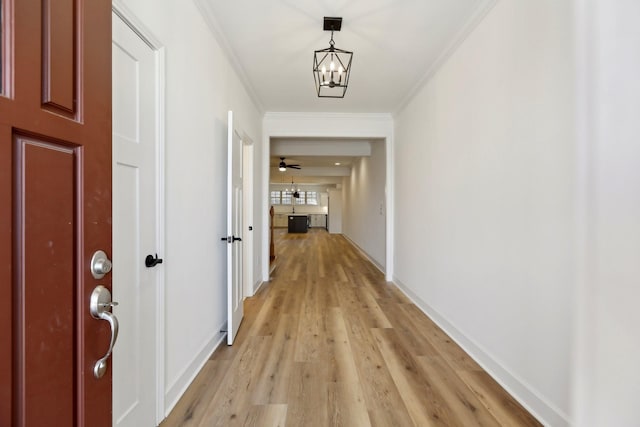 hall with ornamental molding, an inviting chandelier, and light wood-type flooring