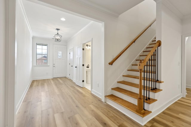 entrance foyer with ornamental molding, an inviting chandelier, and light wood-type flooring