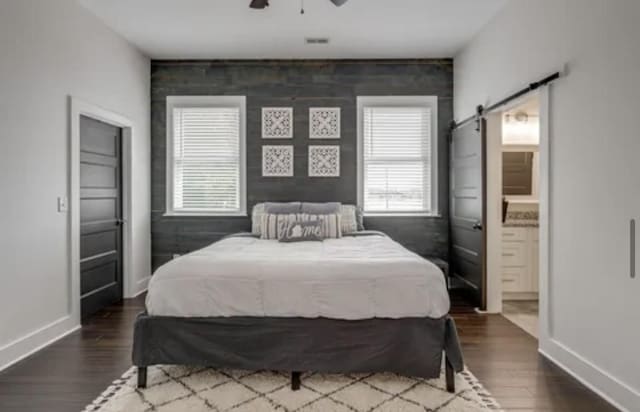 bedroom with wood finished floors, baseboards, and a barn door