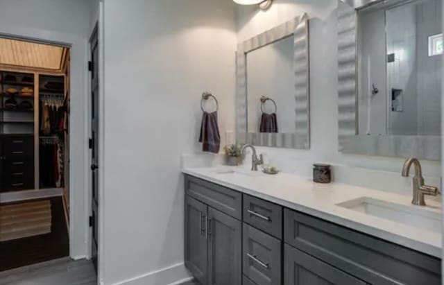 full bath featuring double vanity, a sink, a walk in closet, and baseboards