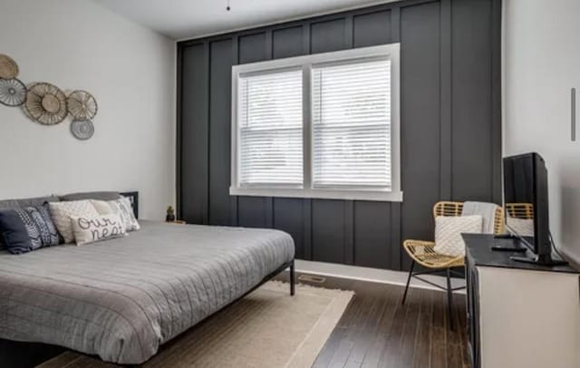 bedroom with dark wood-style floors and a decorative wall