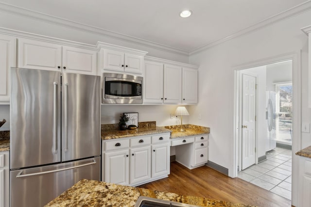 kitchen with white cabinetry, stainless steel appliances, built in desk, and dark stone counters