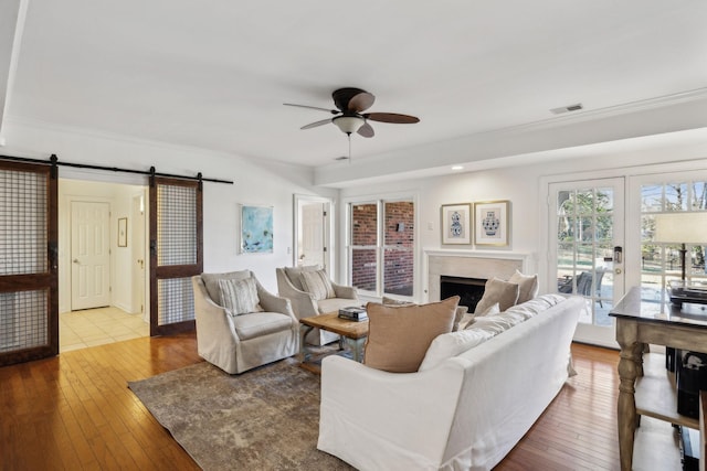 living room featuring hardwood / wood-style flooring, ceiling fan, a barn door, and french doors