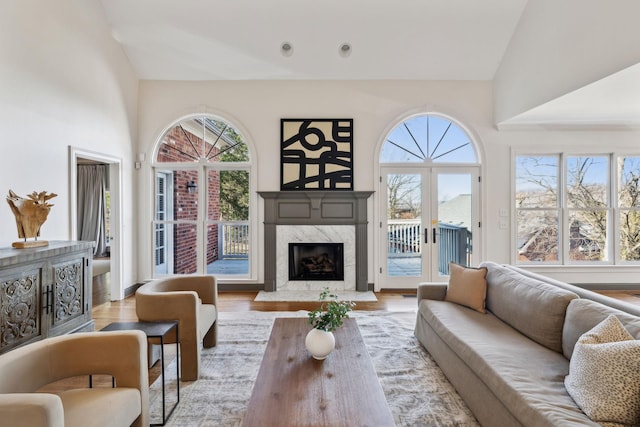 living room with a high end fireplace, high vaulted ceiling, light hardwood / wood-style flooring, and a wealth of natural light