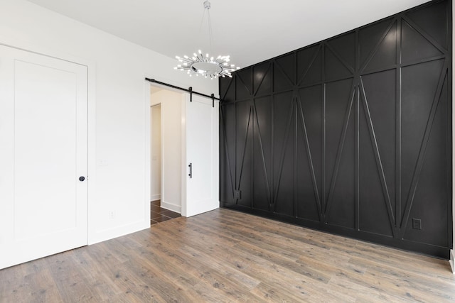 spare room with an inviting chandelier, wood-type flooring, and a barn door