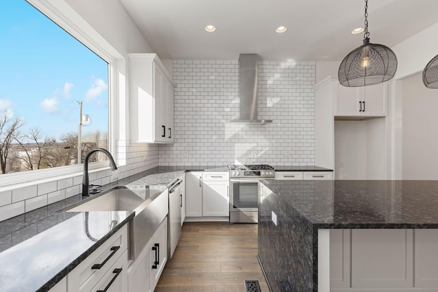 kitchen featuring tasteful backsplash, appliances with stainless steel finishes, wall chimney range hood, and white cabinets