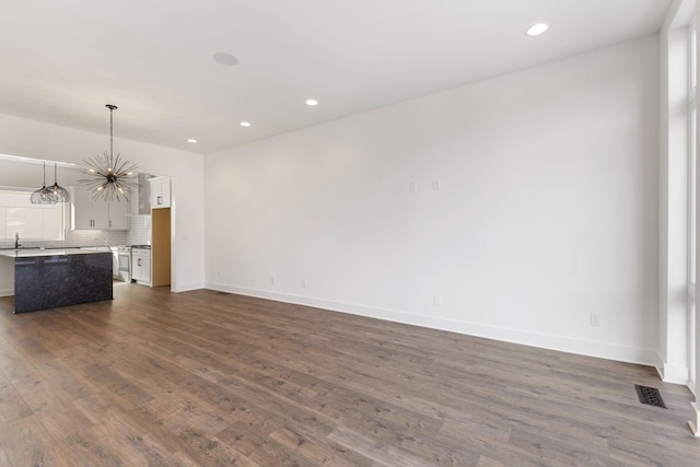 unfurnished living room featuring sink, a notable chandelier, and dark hardwood / wood-style flooring