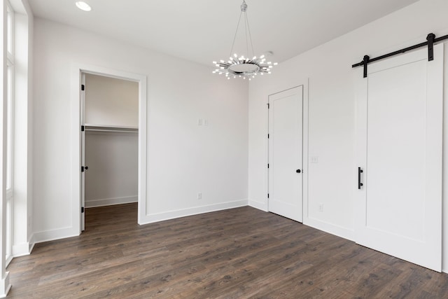 unfurnished bedroom featuring a walk in closet, a barn door, an inviting chandelier, and dark hardwood / wood-style flooring