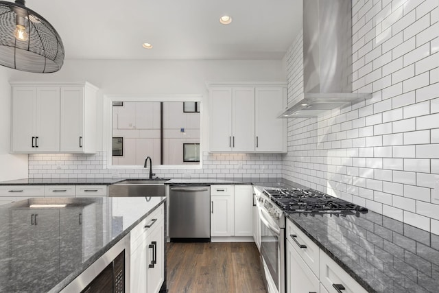 kitchen with sink, appliances with stainless steel finishes, white cabinets, pendant lighting, and wall chimney range hood