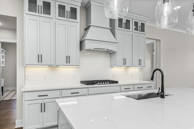 kitchen with premium range hood, stainless steel gas cooktop, sink, light stone countertops, and white cabinets