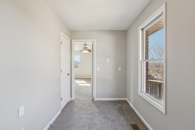 hallway featuring a textured ceiling, light colored carpet, and a healthy amount of sunlight