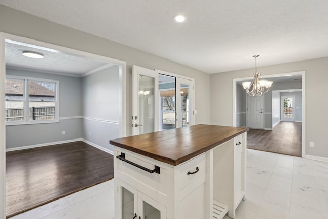 kitchen with butcher block countertops, white cabinetry, a chandelier, a wealth of natural light, and pendant lighting