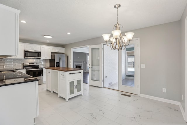 kitchen featuring pendant lighting, backsplash, stainless steel appliances, a center island, and white cabinets