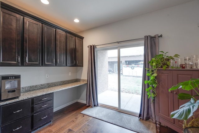 kitchen with light stone counters, dark brown cabinetry, recessed lighting, light wood-style floors, and built in desk