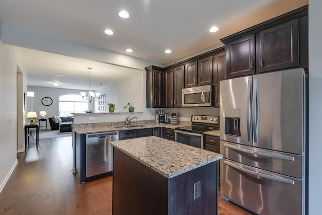 kitchen with light stone counters, appliances with stainless steel finishes, open floor plan, a sink, and dark brown cabinets