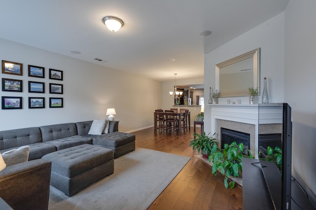 living area with a fireplace, wood finished floors, visible vents, baseboards, and an inviting chandelier