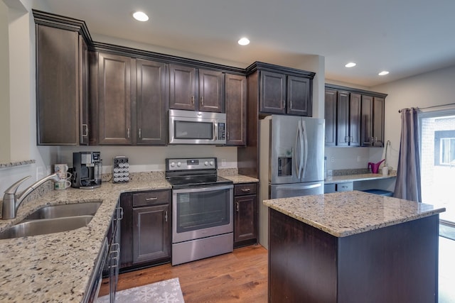 kitchen with light stone counters, light wood-style flooring, appliances with stainless steel finishes, a sink, and dark brown cabinetry