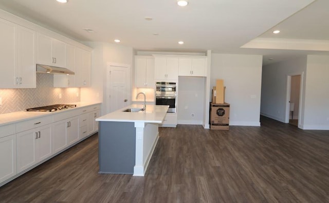 kitchen featuring tasteful backsplash, sink, white cabinets, a kitchen island with sink, and dark wood-type flooring