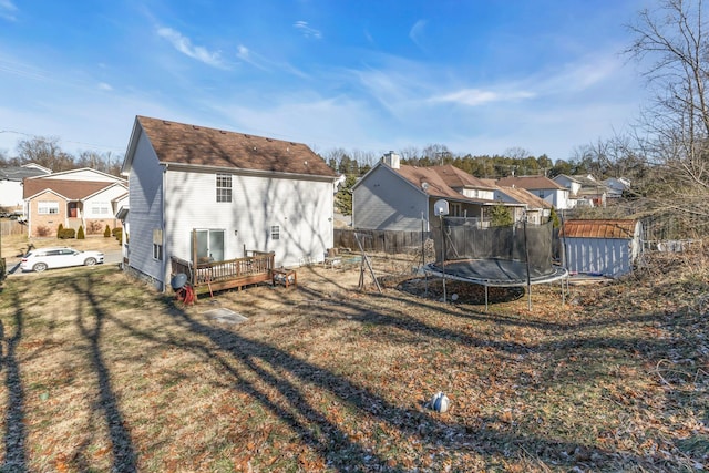 rear view of property featuring a wooden deck, a yard, a trampoline, and a shed