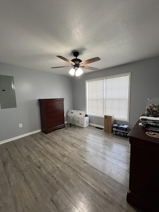 unfurnished bedroom with a textured ceiling, hardwood / wood-style floors, electric panel, and ceiling fan