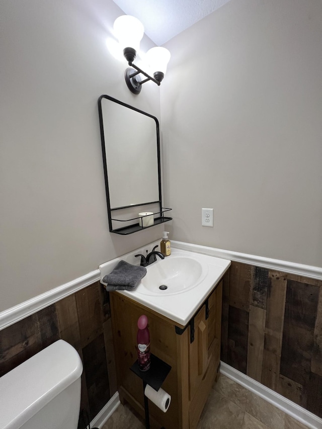 bathroom with vanity, wooden walls, and toilet