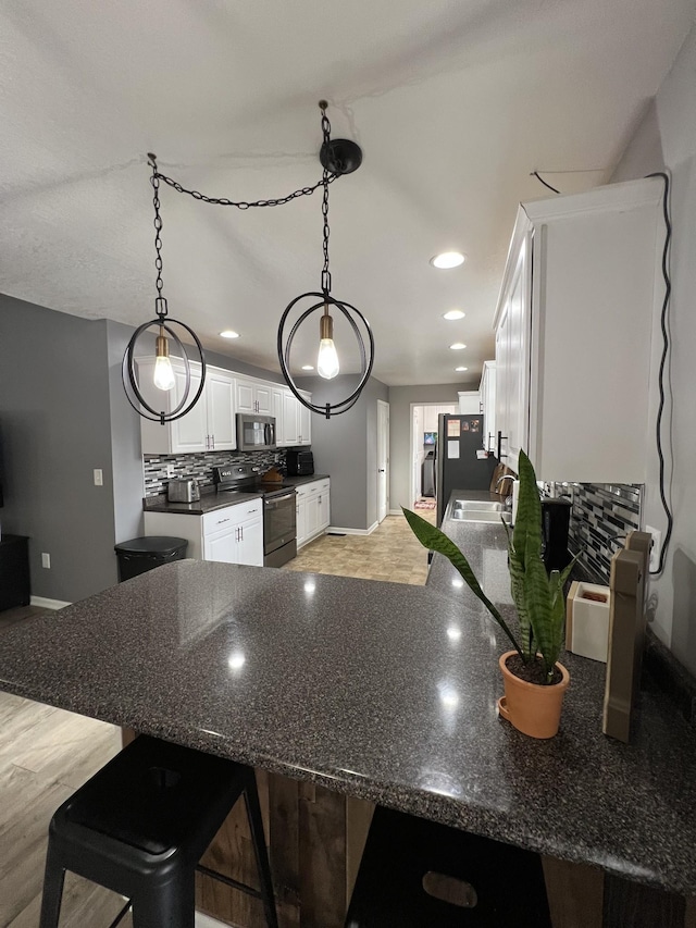 kitchen with white cabinetry, decorative light fixtures, black electric range, and a breakfast bar