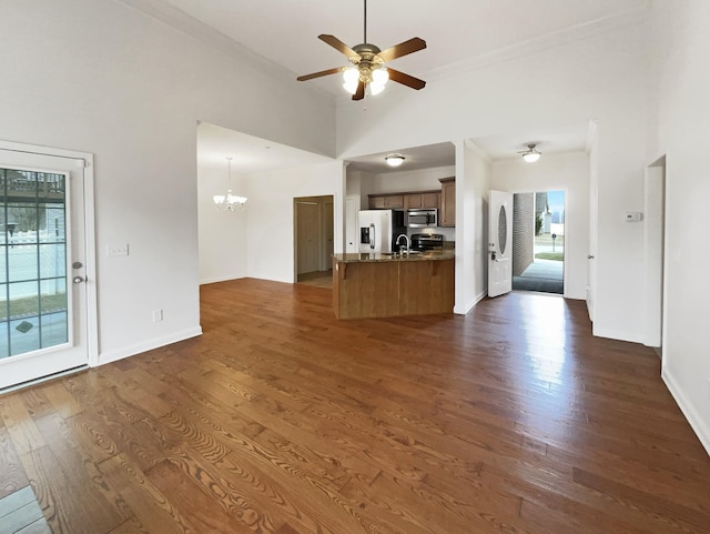 unfurnished living room featuring dark hardwood / wood-style floors, ceiling fan with notable chandelier, a towering ceiling, sink, and ornamental molding