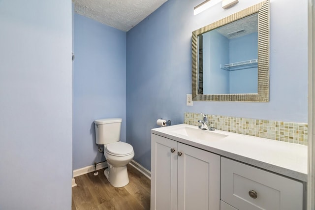 bathroom featuring toilet, wood-type flooring, a textured ceiling, vanity, and backsplash