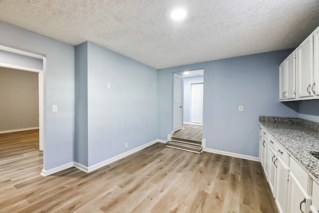 interior space featuring white cabinetry, light hardwood / wood-style flooring, light stone countertops, and a textured ceiling