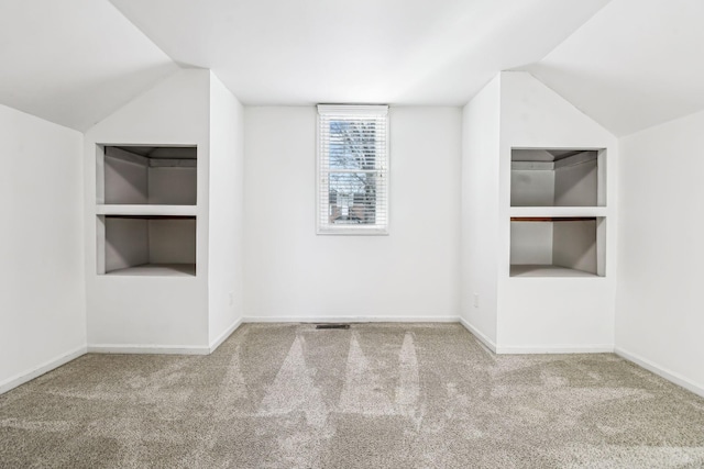 additional living space featuring lofted ceiling, built in shelves, and carpet